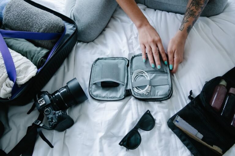 An open fabric travel organizer holding coiled charging cables, a power bank, earbuds, and a plug adapter