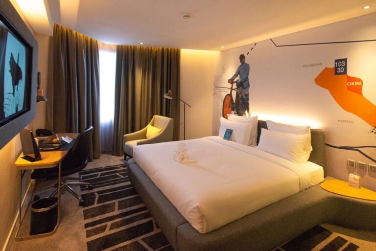 A small hotel room with a double bed and desk, photographed from the doorway so the full width of the room is visible