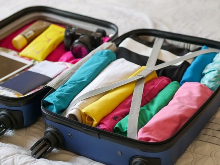 An open suitcase on a bed with clothes folded and rolled inside