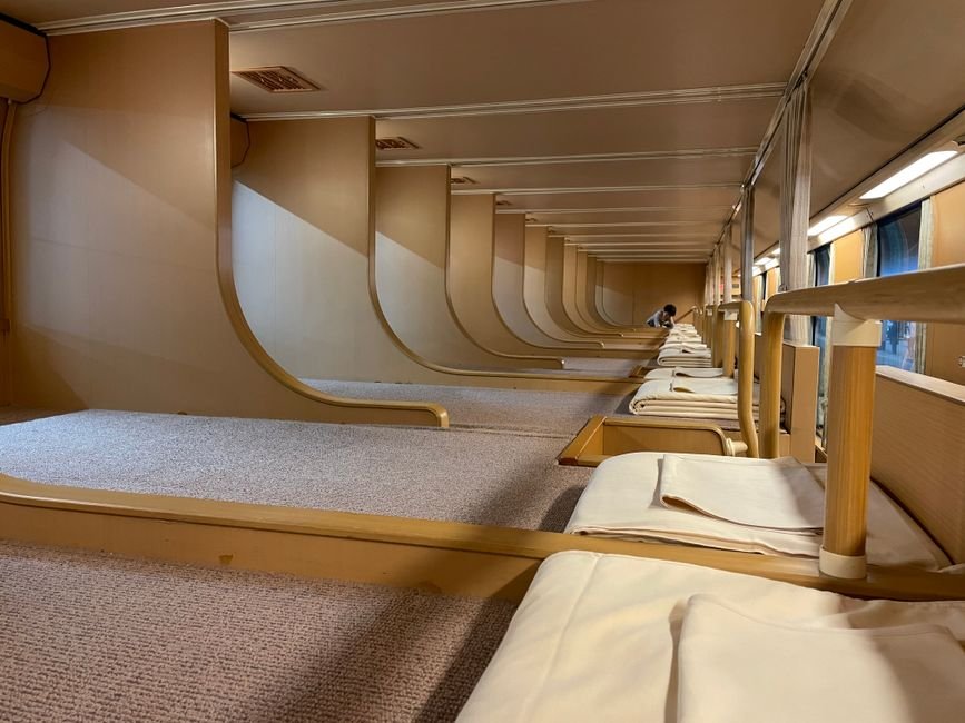 Inside a sleeper train compartment with made-up bunks and a window