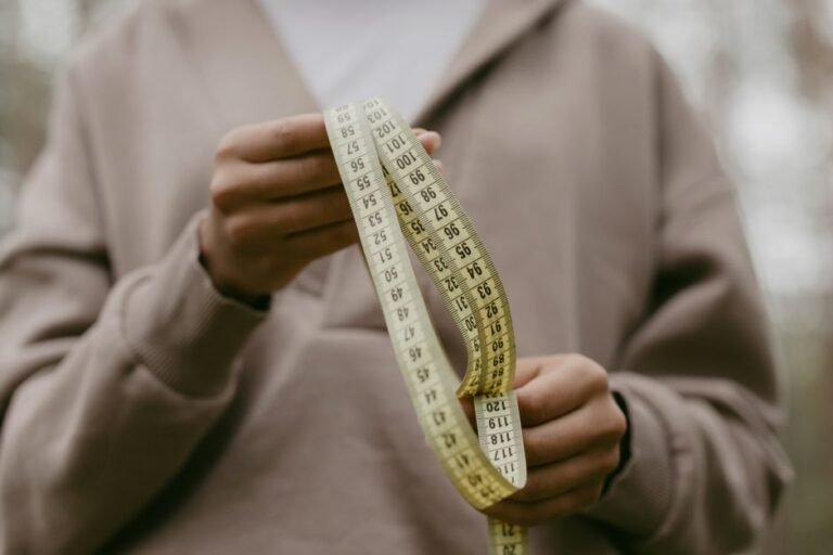 A person measuring their waist with a soft tape measure