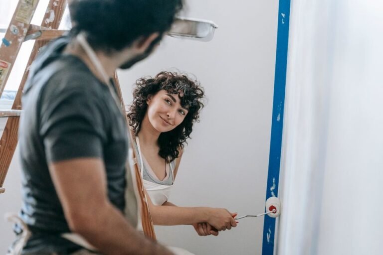 A person rolling paint onto an interior wall with painter's tape along the trim