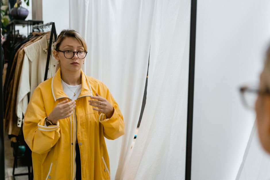 A person trying on a wool winter coat in front of a store mirror
