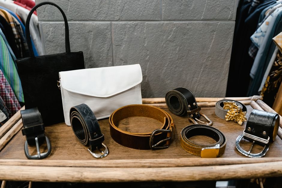 Several leather belts of varying widths laid out side by side on a wooden table