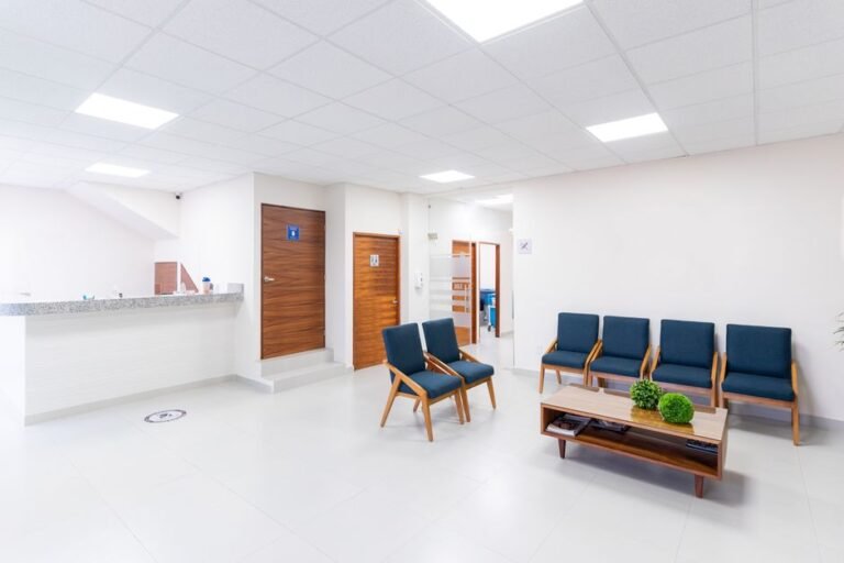 A quiet clinic waiting room with a row of chairs, a reception desk, and health posters on the wall