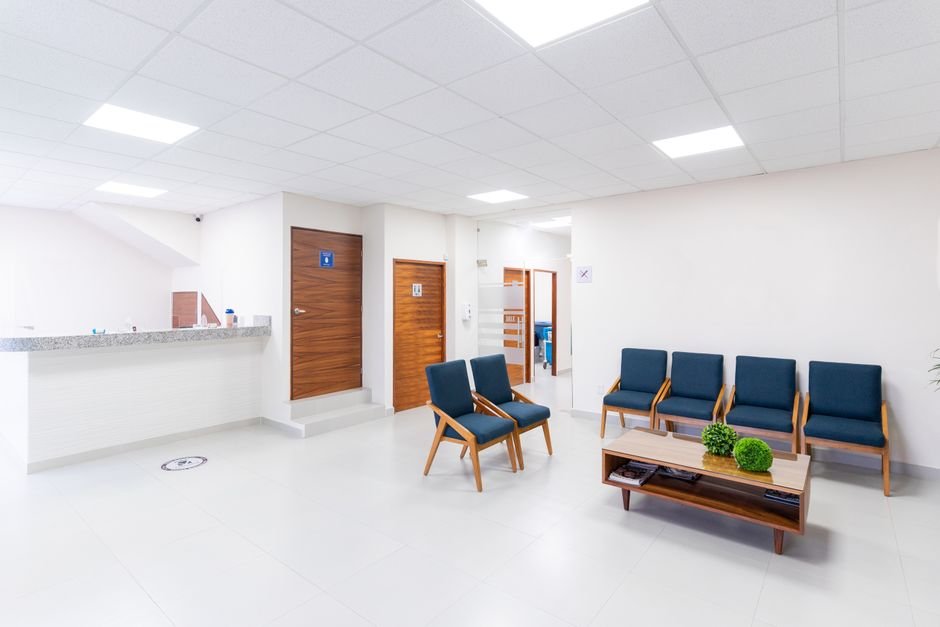 A quiet clinic waiting room with a row of chairs, a reception desk, and health posters on the wall