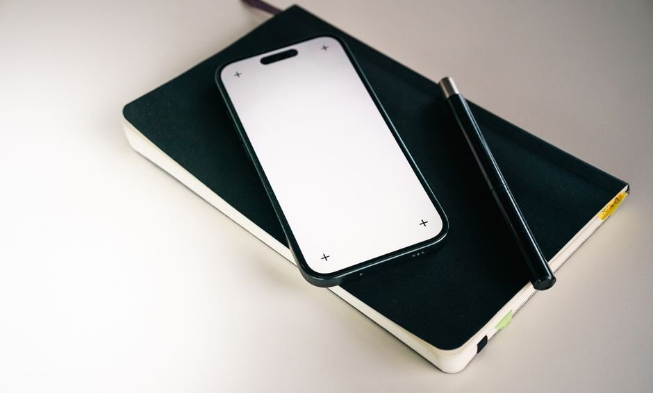 A smartphone showing a travel journal app with a map and photos, resting beside a paper notebook
