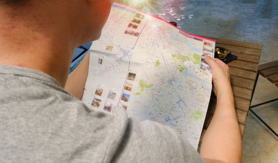 A traveler with a rolling suitcase studying a paper city map on a street corner