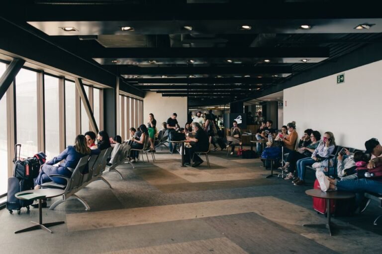 Travelers sitting in armchairs in an airport lounge with large windows overlooking parked aircraft